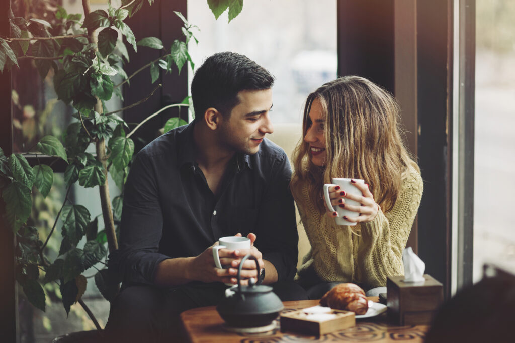A man and a woman drinking coffee and smiling at each other. Tips for a first date.