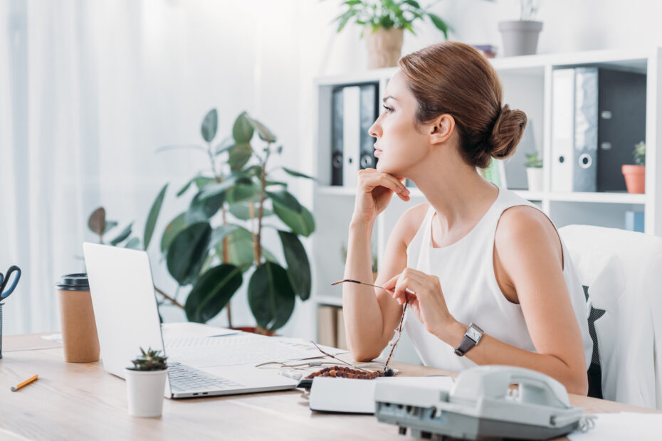 pensive single business woman sitting at workplace with laptop in modern office